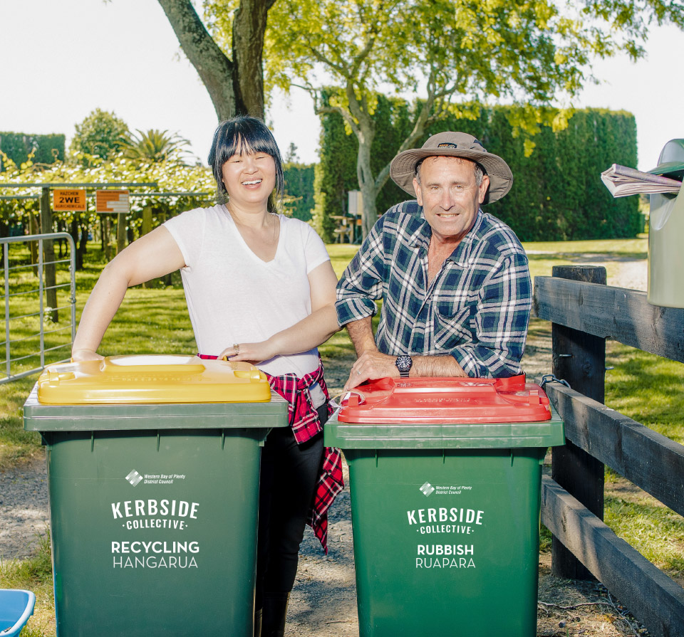 Two farmers leaning over their Western Bay recycling and rubbish bins.
